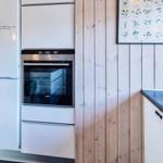Küche mit Kühlschrank, Backofen und Waschmaschine an Holzwand