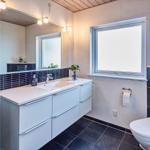 Badezimmer mit Waschbecken, Spiegel und Fenster. Toilette und Fliesenboden.