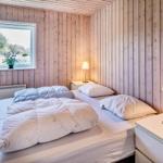 Schlafzimmer mit Holzwand, Bett, Nachttisch und Fenster mit Blick auf Grün.