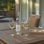 Holztisch mit Weinflasche, zwei Gläsern und Kerzen auf Terrasse.
