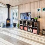 Wohnzimmer mit Holzwand, Kamin und TV-Bereich. Holzdielenboden und große Fenster.
