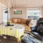 Wohnzimmer mit braunem Sofa, schwarzen Ledersesseln und runden Tisch mit Tischdecke.