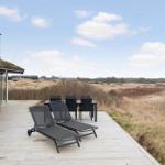 Terrasse mit Liegestühlen und Esstisch. Blick auf trockenes Gras und Himmel.