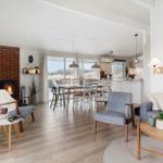 Wohn- und Essbereich mit Kamin, Tisch und Stühlen, Sofa und Couchtisch. Holzboden und große Fenster.