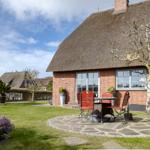 Haus mit Strohdach, Garten und Terrasse mit Tisch und Stühlen.