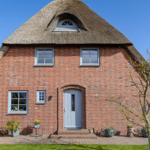 Rotes Backsteingebäude mit Strohdach und blauer Tür.