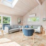 Living room with wood walls, sofa, chairs, and window view of trees.