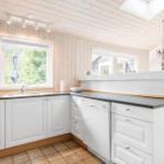 Kitchen with white cabinets, dark worktop, and wooden wall. Windows with garden view.