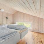 Two beds in a wooden house with sloped ceilings and window view.