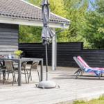 Terrace with table, chairs, and lounge chairs. Background: wooden fence and trees.