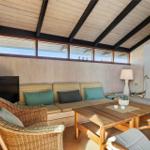 Living room with sofa, fireplace, and wooden table. Ceiling with wood paneling and window row.