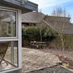 Hinterhof mit Steinplatten, Holzbank und Zaun. Durchgehendes Glasdach über Terrasse.