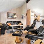 Wohnbereich mit schwarzen Ledersofas und Sesseln, Holzwand und Küchenbereich.