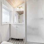 Badezimmer mit Dusche, Waschbecken und Toilette. Weiße Wände und Holzdecke.