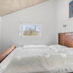 Schlafzimmer mit Holzbett, weißer Wandverkleidung und kleinem Fenster.