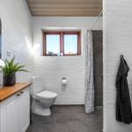 Badezimmer mit Toilette, Dusche, Spiegelschrank und Fenster.
