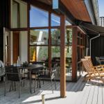 Terrasse mit Tisch, Stühlen und Liegen. Holzdecke und große Fenster.