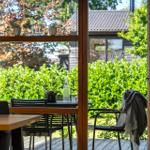 Terrasse mit Tisch, Stühlen und Decke. Blick auf grüne Hecke und Haus.