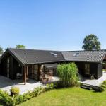 Moderne Holzhütte mit Terrasse und Garten unter blauem Himmel.