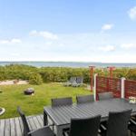 Terrasse mit Tisch und Stühlen, Blick auf Grünflächen und Meer.