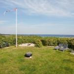 Grüner Garten mit Liegestühlen, Feuerplatz und Blick aufs Meer.