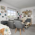Wohn- und Essbereich mit grauem Sofa, Tisch und Stühlen. Weiße Wände und Fenster mit Blick.