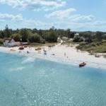 Strand mit weißem Sand, klarem Wasser und einigen Menschen.