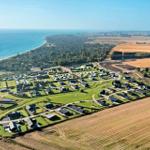 Luftbild eines Ferienplatzes mit Häusern, Grünflächen und Meer im Hintergrund.