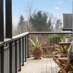 Terrasse mit Holzbank, Pflanzen und Tisch. Blick auf Bäume und Himmel.