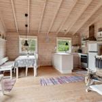 Holzhaus mit Küche, Esstisch und Sitzgelegenheiten. Weiße Möbel und Fenster.