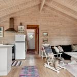 Wohnküche mit Holzwand und -decke, weißer Kühlschrank und Sitzgelegenheiten.