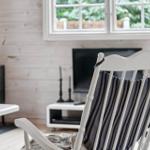 Ein weißer Sessel mit Streifenkissen steht vor einem Fenster. Im Hintergrund ist ein Kaminofen mit brennendem Feuer.
