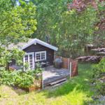 Holzhaus mit Terrasse im Grünen, umgeben von Bäumen und Sträuchern.