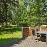 Terrasse mit Tisch und Stühlen unter Bäumen. Grasfläche und Zaun im Hintergrund.