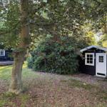 Zwei schwarze Hütten mit weißen Fenstern und Türen im Wald. Gras und Bäume umgeben die Gebäude.