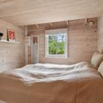 Schlafzimmer mit Holzwand, Bett und Fenster mit Blick auf Grün.