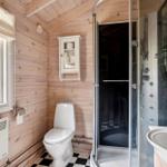 Badezimmer mit Dusche, Toilette und Waschbecken. Holzwände und schwarz-weißes Fliesenboden.