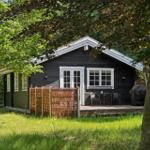 Holzhütte mit Terrasse, umgeben von Bäumen und Gras.