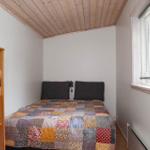 Schlafzimmer mit Bett, Bücherregal und Fenster. Holzdecke und gemustertes Bettlaken.