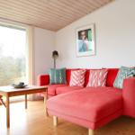 Ein Wohnzimmer mit rotem Sofa, Holzboden und großem Fenster zur Außenseite.