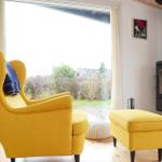 Gelber Sessel und Hocker neben Kamin und Fenster mit Blick auf Garten.