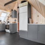Küche mit grauen Schränken, weißem Kühlschrank und Holzwänden unter Dachschrägen.