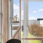 Ein Fernrohr auf Stativ neben einem Fenster mit Blick auf Gras und Himmel.