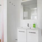 Badezimmer mit Waschbecken, Spiegel und Dusche. Handtuch hängt an Wand.