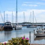 Hafen mit Segelyachten und kleinen Booten unter blauem Himmel.
