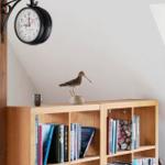 Holzregal mit Büchern, Vogeldekoration und Wanduhr an schräger Wand.