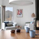 Wohnraum mit Kamin, Sofa und großem Fenster. Tisch mit Tassen und Deko.