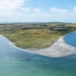 Insel mit grünen Flächen und sandigem Ufer, umgeben von klarem Wasser.