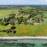 Aeriale Aufnahme einer ländlichen Siedlung am Strand mit grünen Feldern und Bäumen.