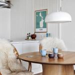Runder Holztisch mit Stühlen und Felldecken. Wandbild und Pendelleuchte.
